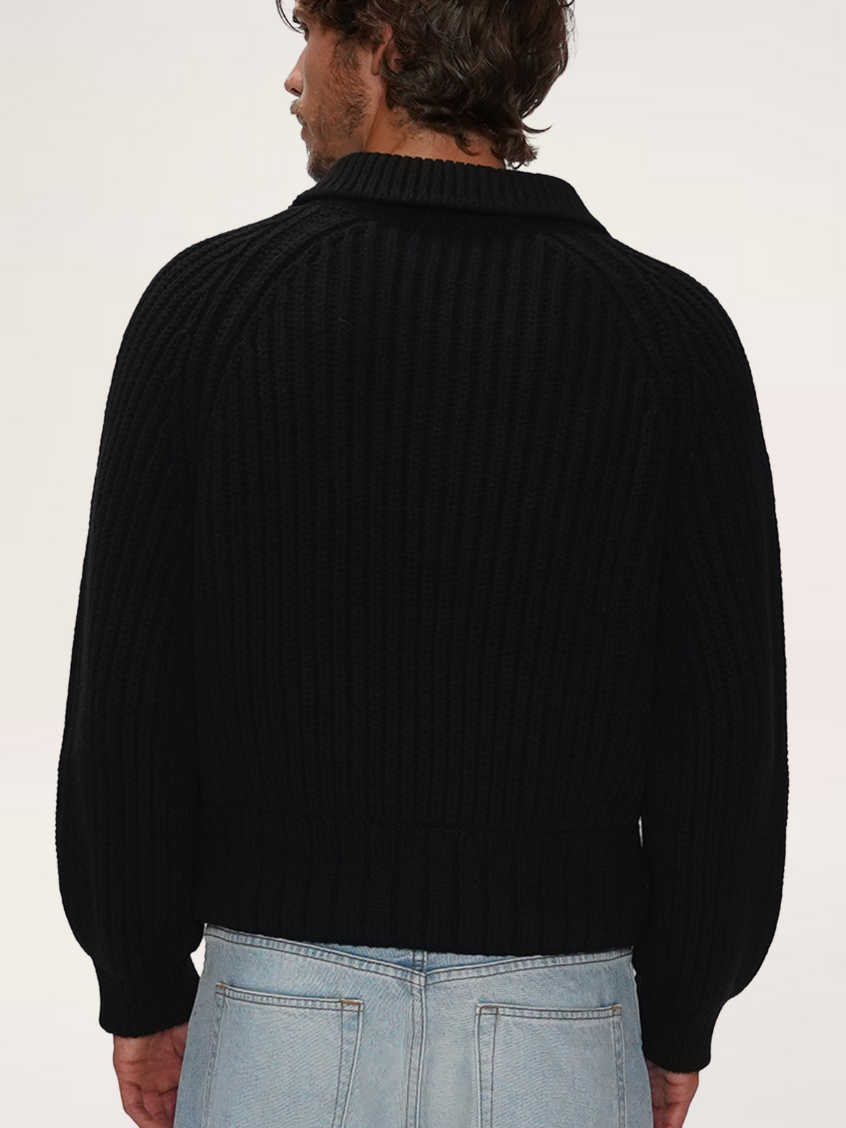 Rear view of a male model wearing a TENDLER black heavyweight half-zip knit sweater with the collar folded.